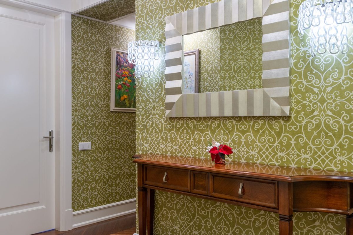 Elegant hallway with green damask wallpaper, a striped-framed mirror and a wooden console table