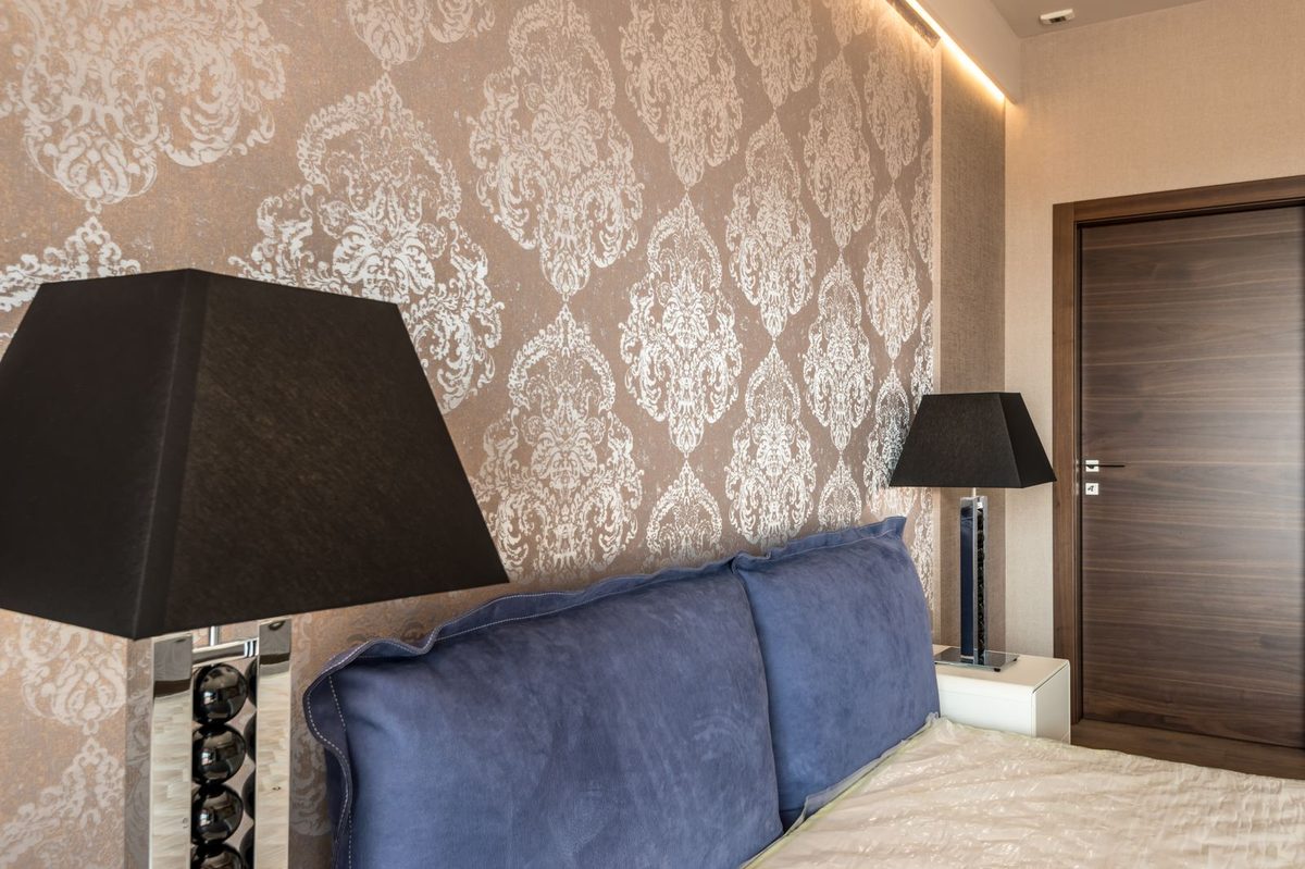 Bedroom with silver-and-white damask wallpaper behind the bed and black bedside lamps