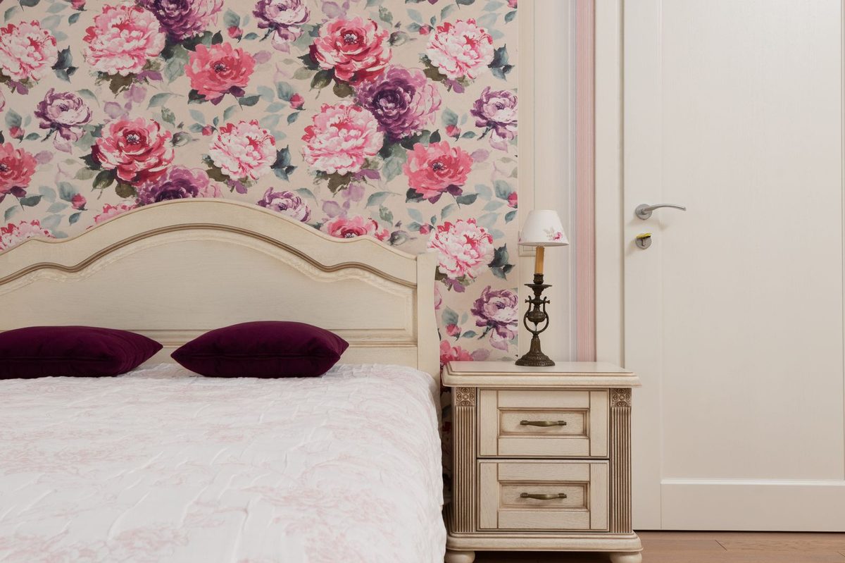 Bedroom with a pink rose floral wallpaper feature wall above a carved headboard