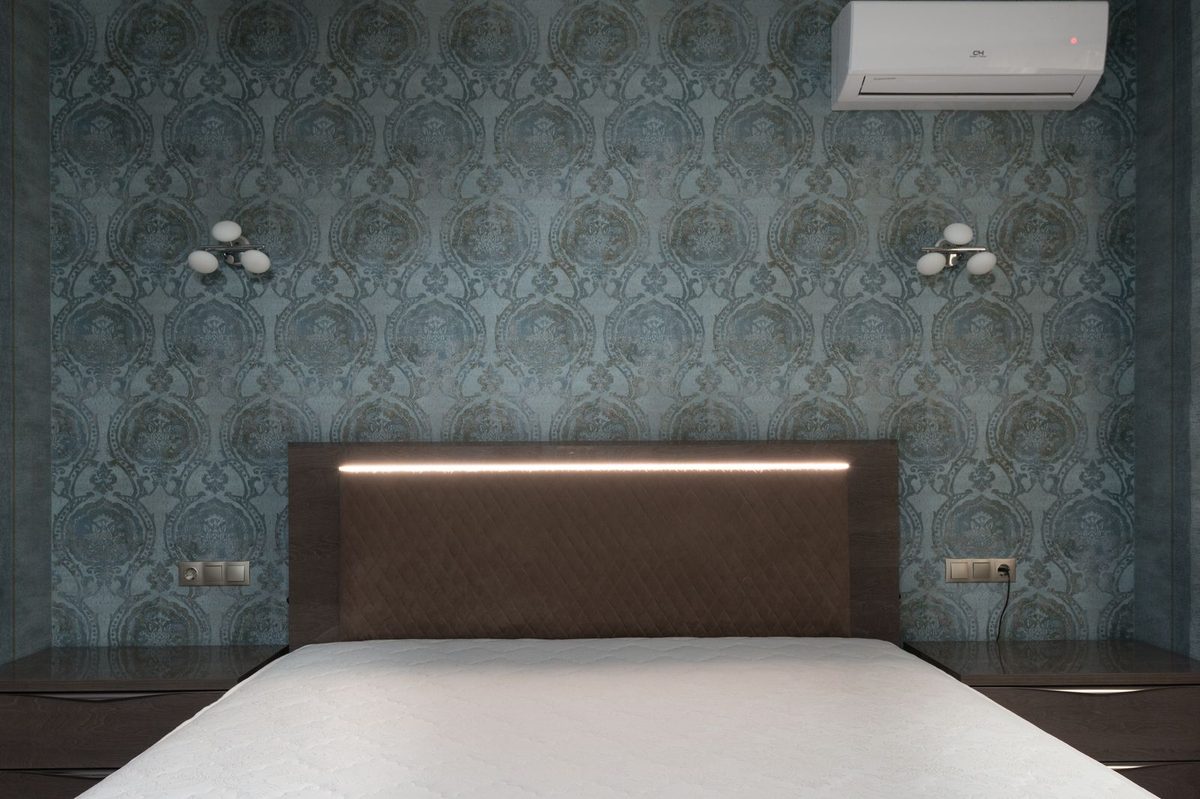 Bedroom with a dimensional teal patterned wallpaper accent wall behind an upholstered headboard
