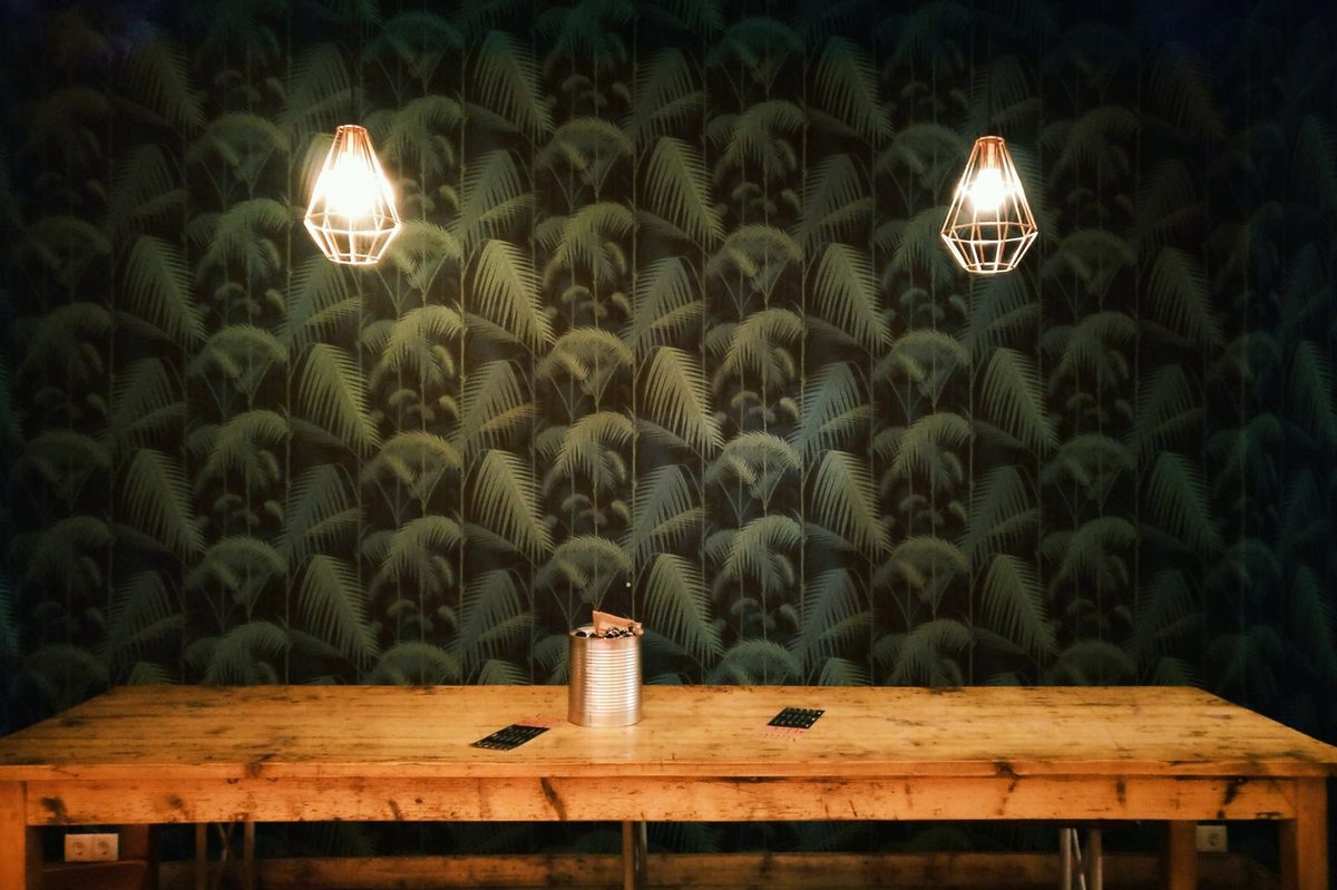 Deep green palm-leaf wallpaper feature wall above a wooden table with geometric pendant lamps